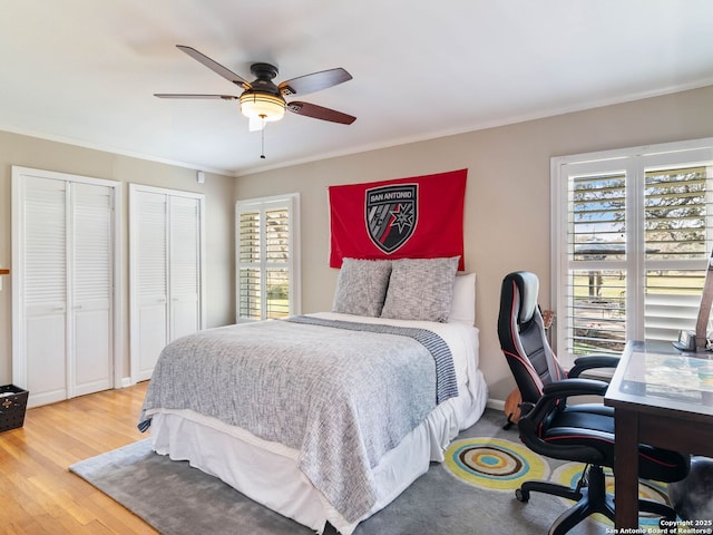 bedroom featuring ornamental molding, a ceiling fan, multiple closets, and wood finished floors