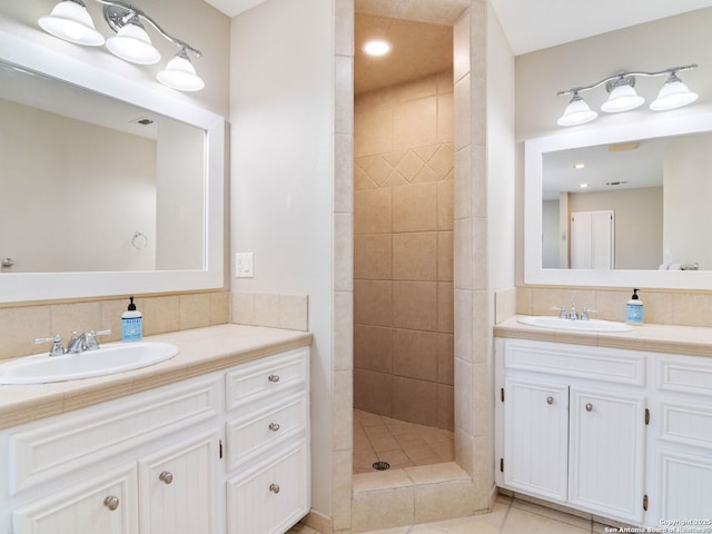 bathroom featuring two vanities, tiled shower, backsplash, and a sink