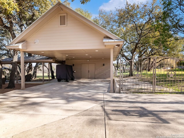 garage featuring a carport, concrete driveway, and a gate