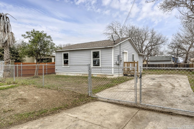 view of side of home with a fenced front yard, a gate, a shingled roof, and concrete driveway