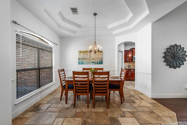 dining area with arched walkways, a raised ceiling, visible vents, and stone tile floors