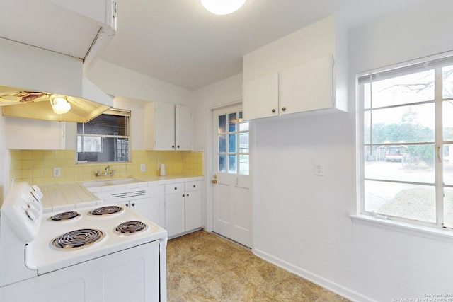 kitchen with white range with electric stovetop, tile countertops, backsplash, white cabinetry, and a sink