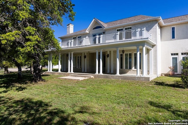 rear view of house featuring covered porch, brick siding, a yard, and a balcony