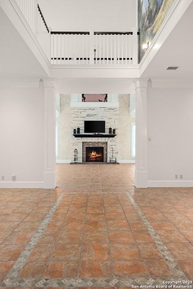 unfurnished living room featuring ornamental molding, a brick fireplace, a high ceiling, and baseboards