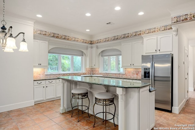 kitchen with backsplash, stainless steel refrigerator with ice dispenser, a kitchen island, and white cabinetry