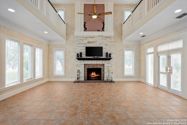 unfurnished living room featuring a high ceiling, a fireplace, visible vents, baseboards, and crown molding