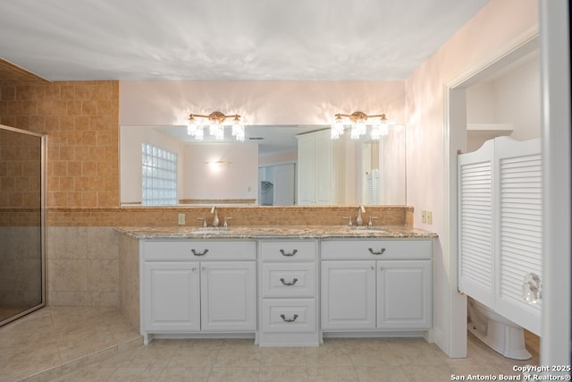 full bathroom with a sink, a tile shower, and double vanity