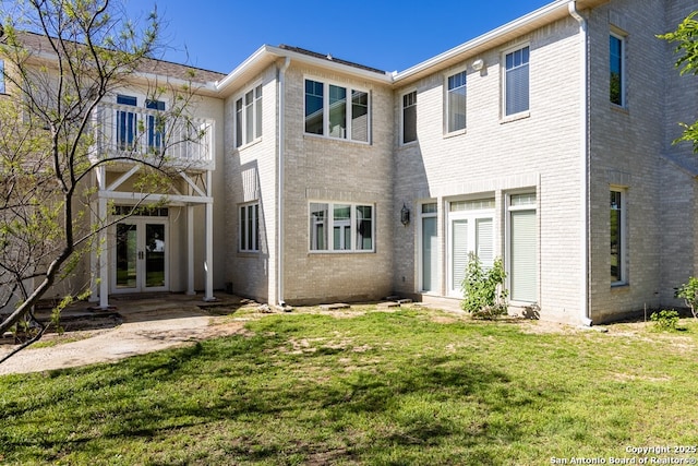 rear view of house with a balcony, brick siding, a lawn, and french doors