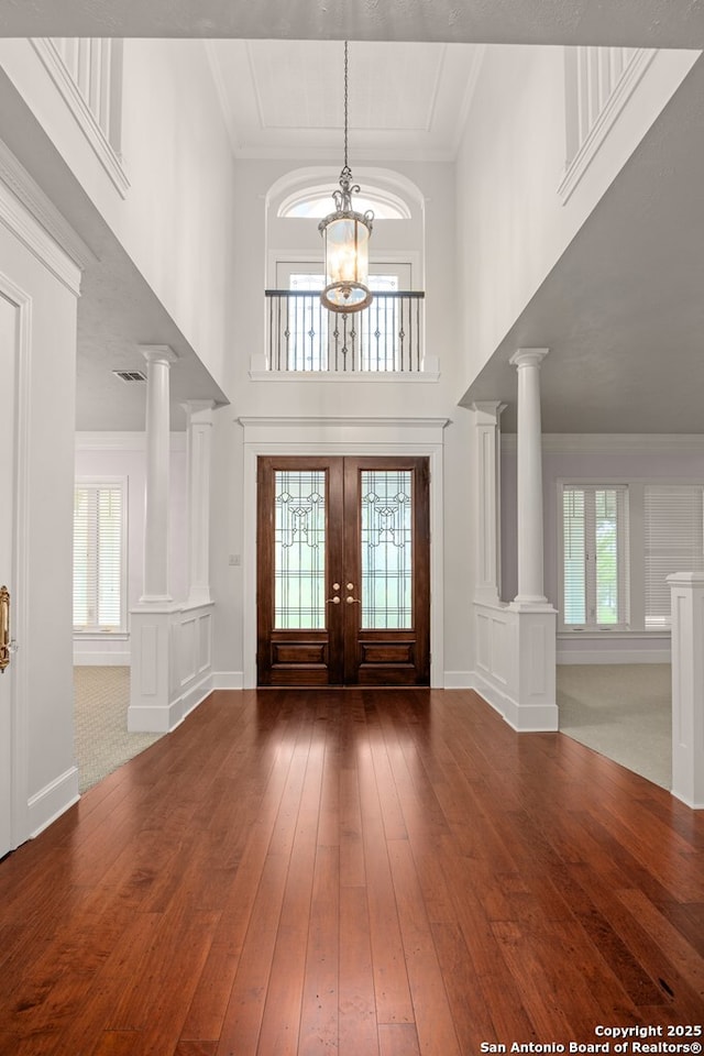 foyer entrance featuring a notable chandelier, french doors, wood-type flooring, decorative columns, and crown molding