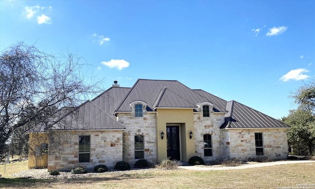 french country style house featuring metal roof, a front lawn, a standing seam roof, and a chimney