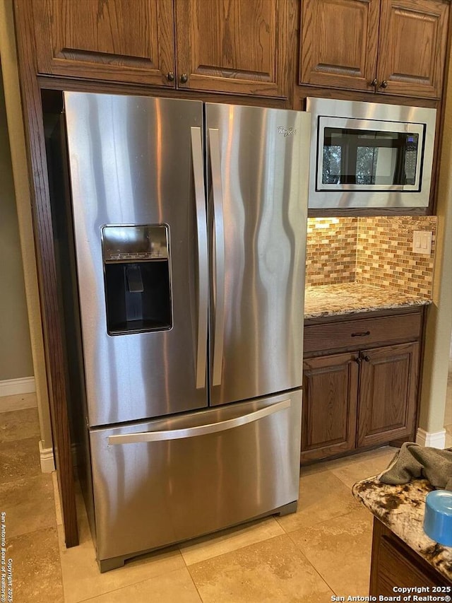 kitchen featuring stainless steel appliances, brown cabinets, backsplash, and light stone countertops