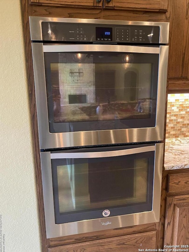 interior details with a textured wall, double oven, tasteful backsplash, and brown cabinetry