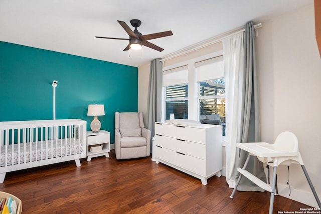 bedroom with a crib, wood finished floors, baseboards, and ceiling fan