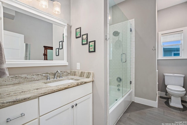 bathroom featuring vanity, toilet, baseboards, and shower / bath combination with glass door