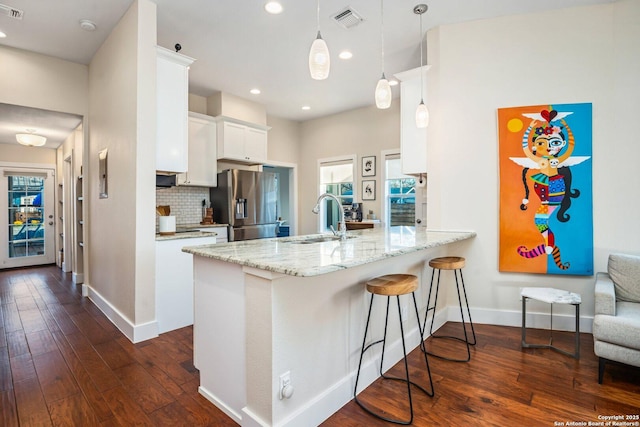 kitchen with visible vents, a sink, tasteful backsplash, stainless steel fridge, and a peninsula