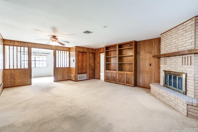 unfurnished living room with light colored carpet, visible vents, a fireplace, and wooden walls