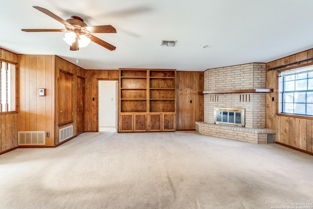 unfurnished living room featuring a brick fireplace, visible vents, and wooden walls