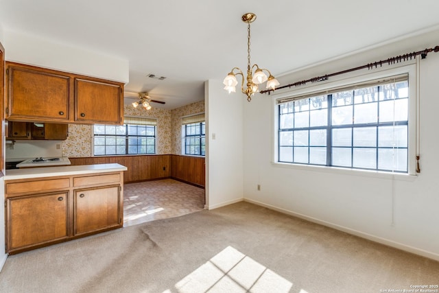 kitchen featuring brown cabinets, a wainscoted wall, light colored carpet, visible vents, and wallpapered walls