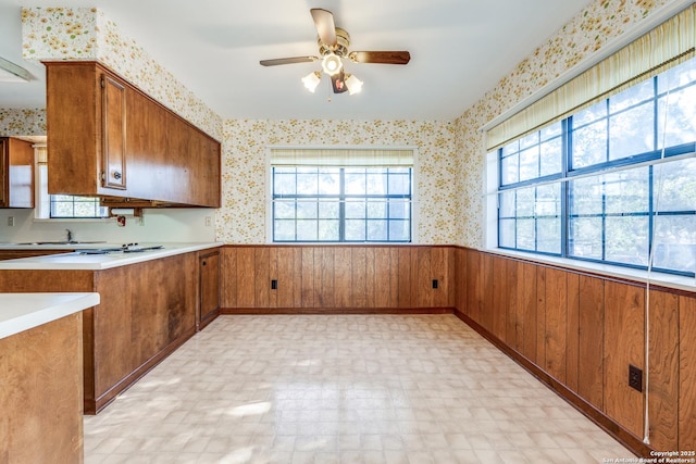 kitchen with brown cabinets, a wainscoted wall, light countertops, wooden walls, and wallpapered walls