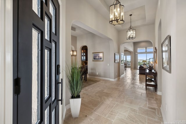 entryway featuring stone tile floors, baseboards, arched walkways, a high ceiling, and a notable chandelier