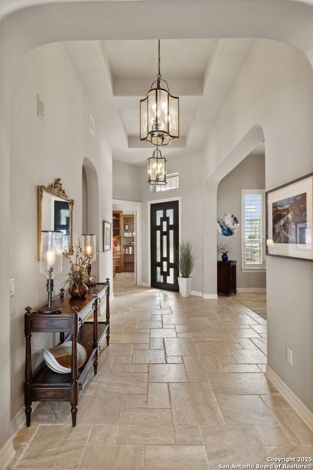 foyer entrance with an inviting chandelier, stone tile floors, baseboards, and a raised ceiling