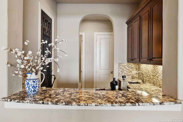 kitchen with arched walkways, stone countertops, a peninsula, a sink, and tasteful backsplash