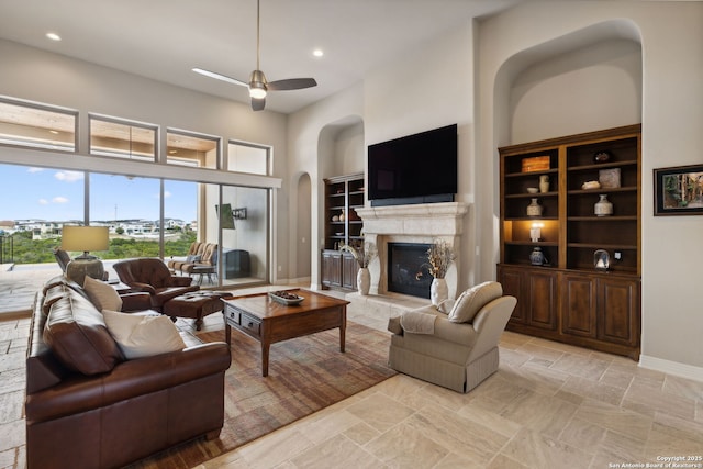 living area featuring ceiling fan, arched walkways, a fireplace, a towering ceiling, and baseboards