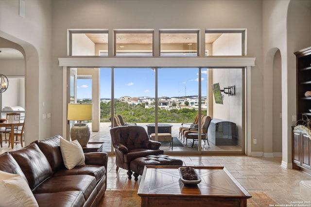 living room with an inviting chandelier, baseboards, arched walkways, and stone tile flooring