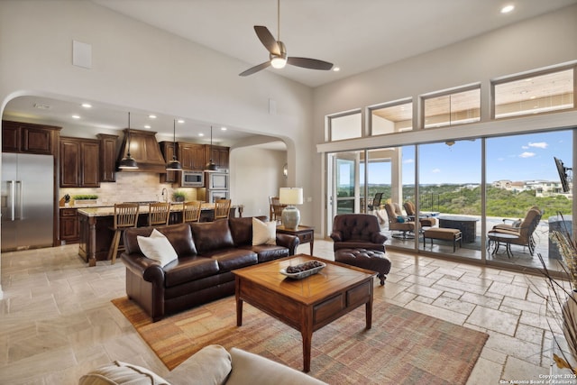 living room with arched walkways, recessed lighting, a towering ceiling, and stone tile floors