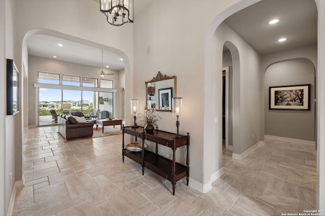 corridor with a towering ceiling, stone tile floors, baseboards, and recessed lighting