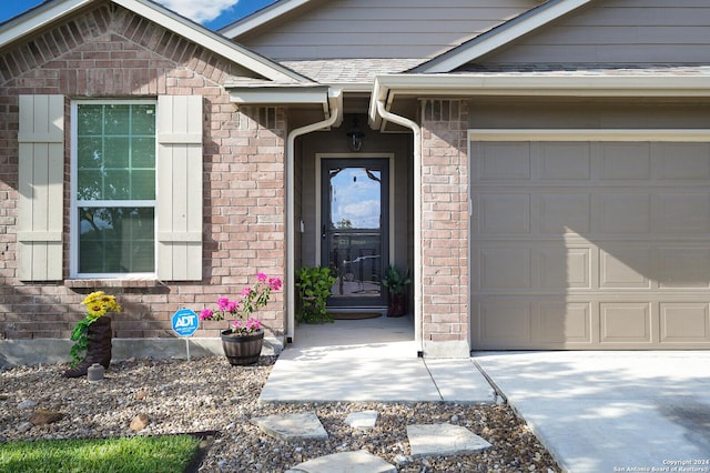 doorway to property with a garage, brick siding, and a shingled roof