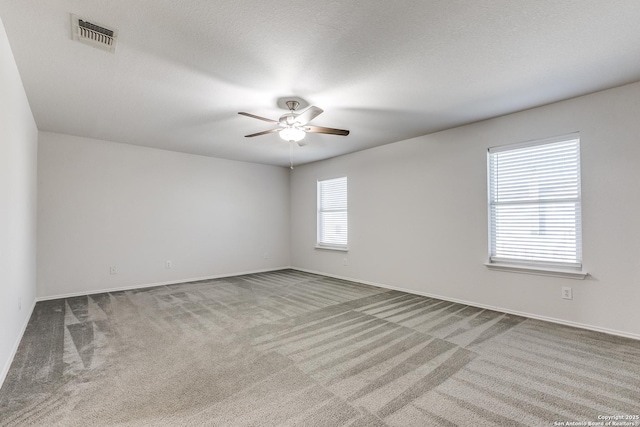 spare room with a textured ceiling, carpet flooring, visible vents, and a ceiling fan