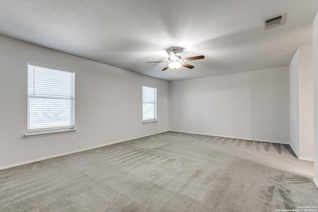 carpeted empty room with visible vents, ceiling fan, a textured ceiling, and baseboards