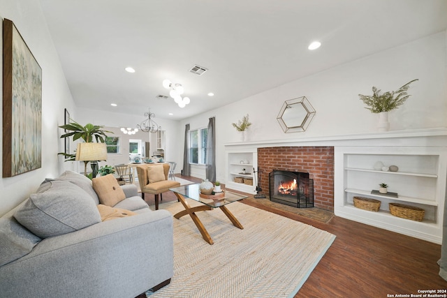 living area with a chandelier, a fireplace, wood finished floors, visible vents, and built in features