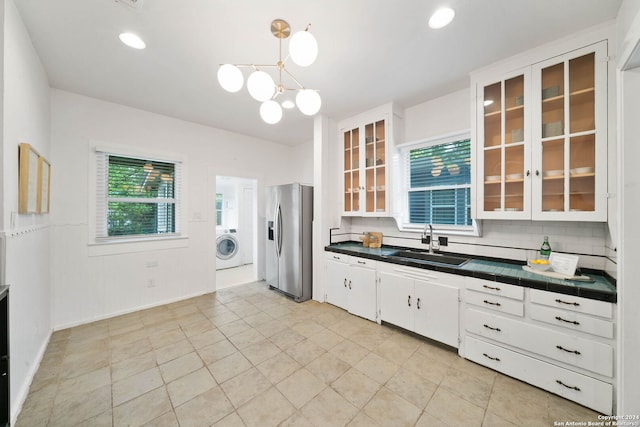 kitchen featuring decorative backsplash, tile countertops, washer / clothes dryer, stainless steel refrigerator with ice dispenser, and a sink