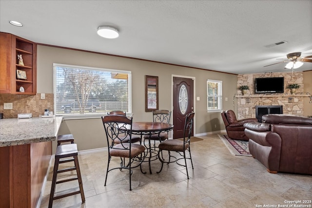 dining area featuring visible vents, baseboards, a ceiling fan, crown molding, and a fireplace