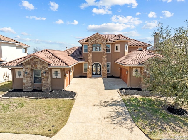 mediterranean / spanish-style home featuring stone siding, a tile roof, concrete driveway, and a front yard