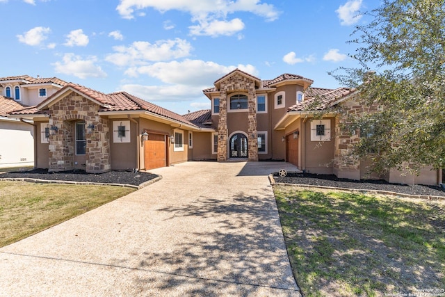 mediterranean / spanish-style house featuring driveway, stone siding, a tiled roof, an attached garage, and stucco siding