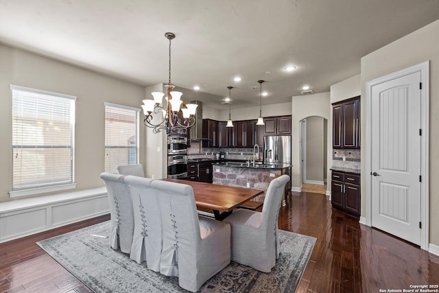 dining area featuring arched walkways, a chandelier, dark wood-type flooring, and recessed lighting