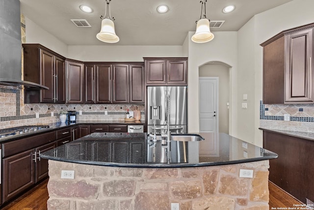 kitchen featuring wall chimney range hood, visible vents, appliances with stainless steel finishes, and arched walkways