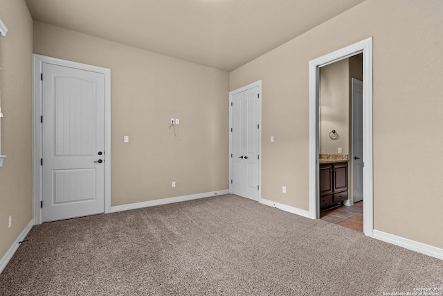 unfurnished bedroom with baseboards, ensuite bath, and light colored carpet