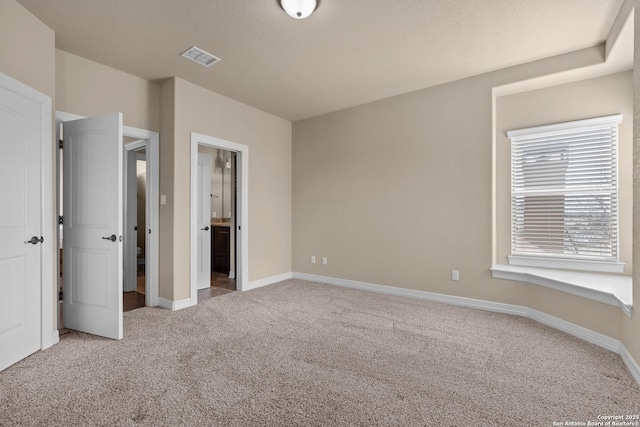 unfurnished bedroom with baseboards, ensuite bath, visible vents, and light colored carpet