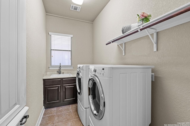 washroom with a textured wall, a sink, visible vents, washer and dryer, and cabinet space