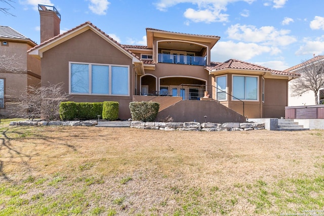 rear view of property featuring a balcony, a tile roof, a lawn, stucco siding, and a chimney