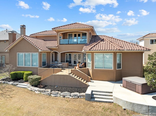 back of property featuring a patio, a balcony, french doors, stucco siding, and a hot tub