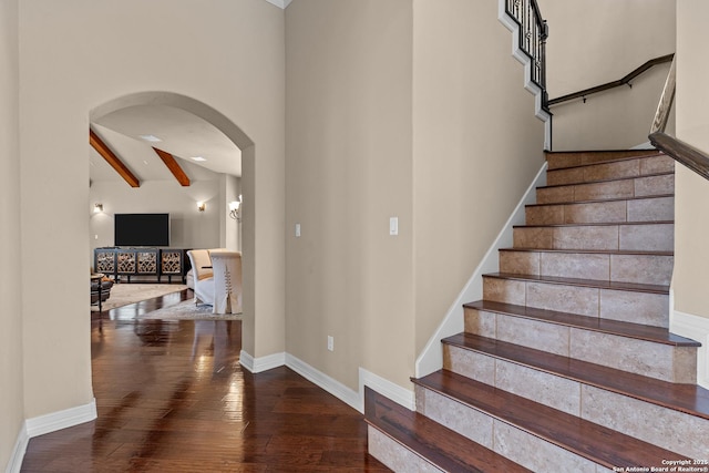 stairway with arched walkways, beamed ceiling, hardwood / wood-style flooring, and baseboards