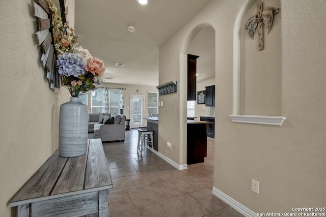 hallway featuring arched walkways, tile patterned flooring, visible vents, and baseboards