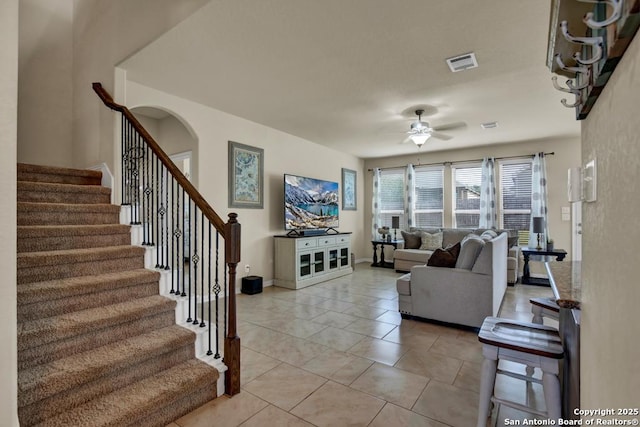 living room featuring light tile patterned floors, baseboards, visible vents, a ceiling fan, and stairs