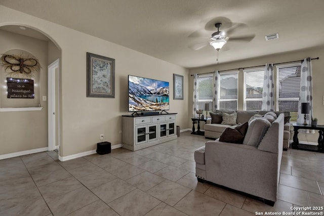 living area featuring arched walkways, light tile patterned flooring, visible vents, baseboards, and a ceiling fan