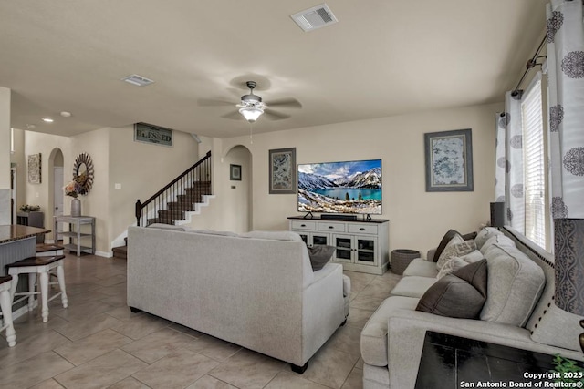 living room with stairway, visible vents, arched walkways, and ceiling fan